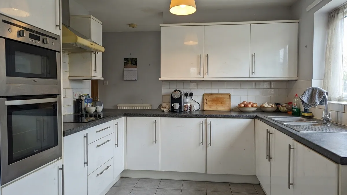 A dated U-shaped kitchen with high-gloss cream cabinets, a dark speckled countertop and cream metro tiles
