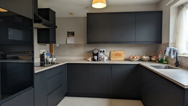 The same U-shaped kitchen with matte black handleless fronts, a light stone-look countertop and backsplash, and new large beige floor tiles