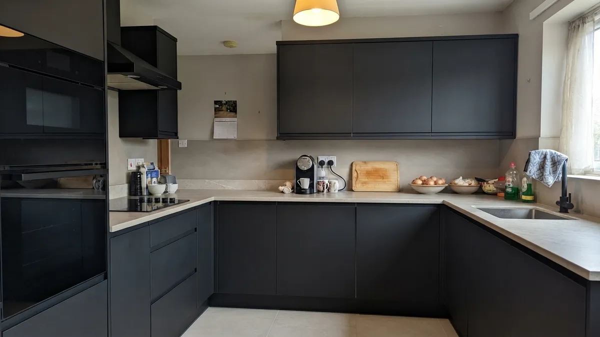 The same U-shaped kitchen with matte black handleless fronts, a light stone-look countertop and backsplash, and large beige floor tiles