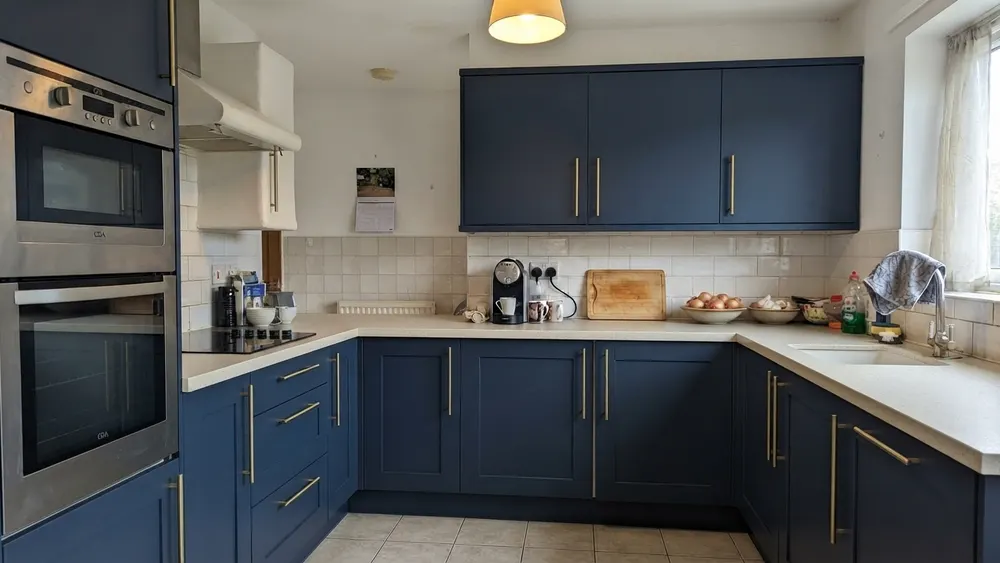 A kitchen with deep navy blue shaker cabinet fronts and a creamy white countertop, with the original floor and tile unchanged