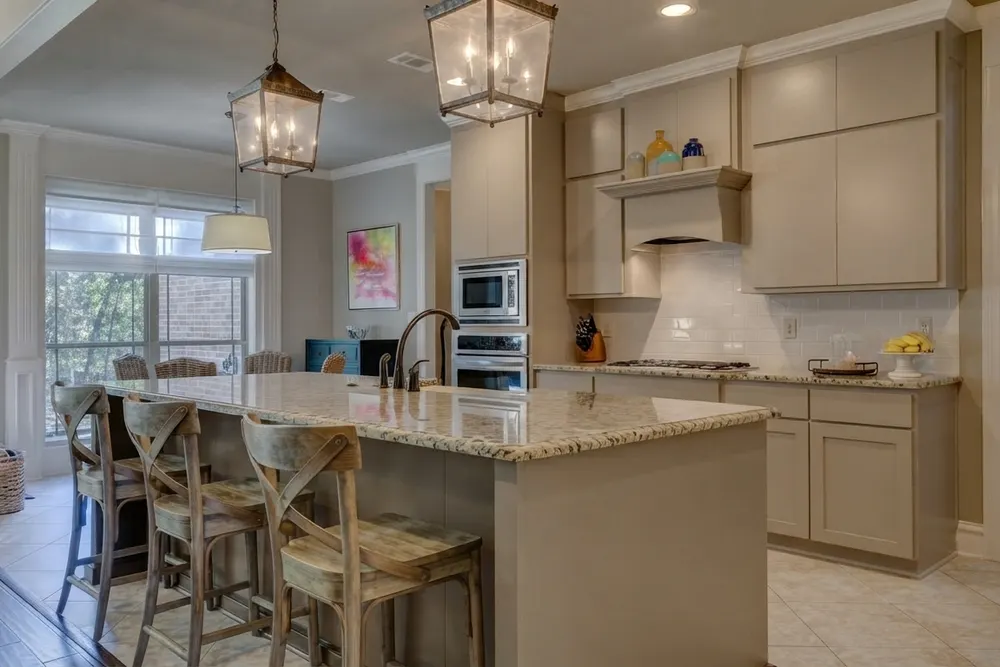 Open kitchen with greige cabinets, speckled light granite countertops and island, and a white glossy subway tile backsplash under a wood range hood
