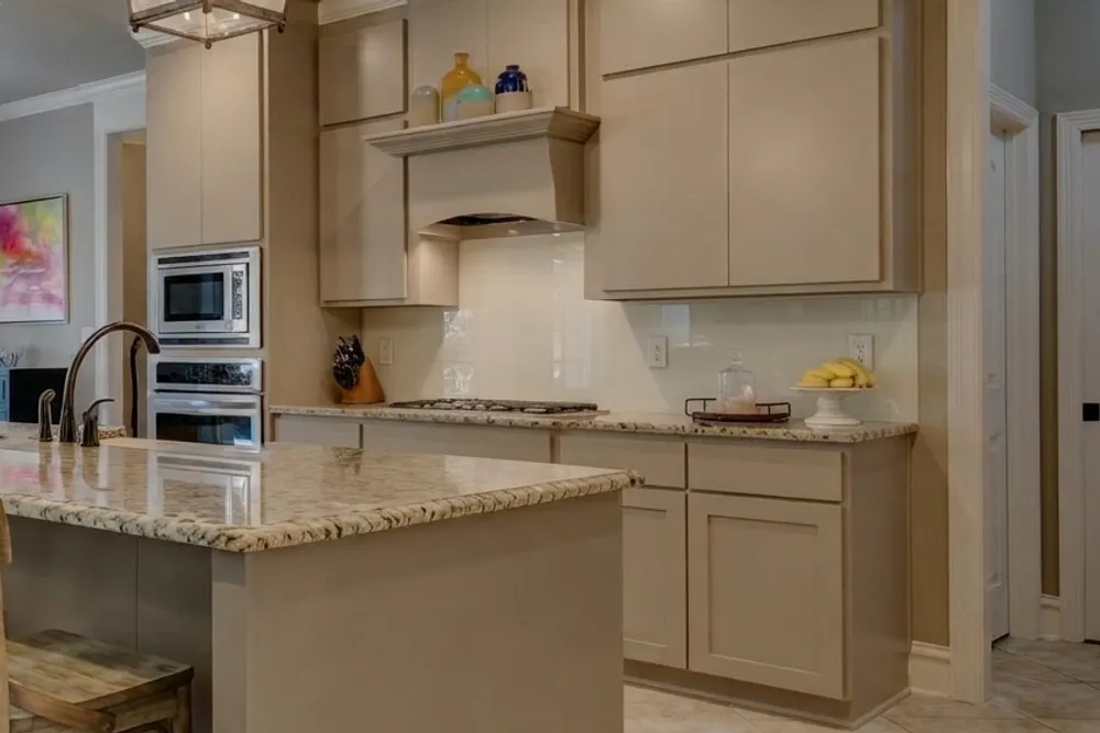 Close-up of the backsplash wall in cream back-painted glass above the speckled granite countertop, with one vertical panel seam visible and the under-cabinet light reflected