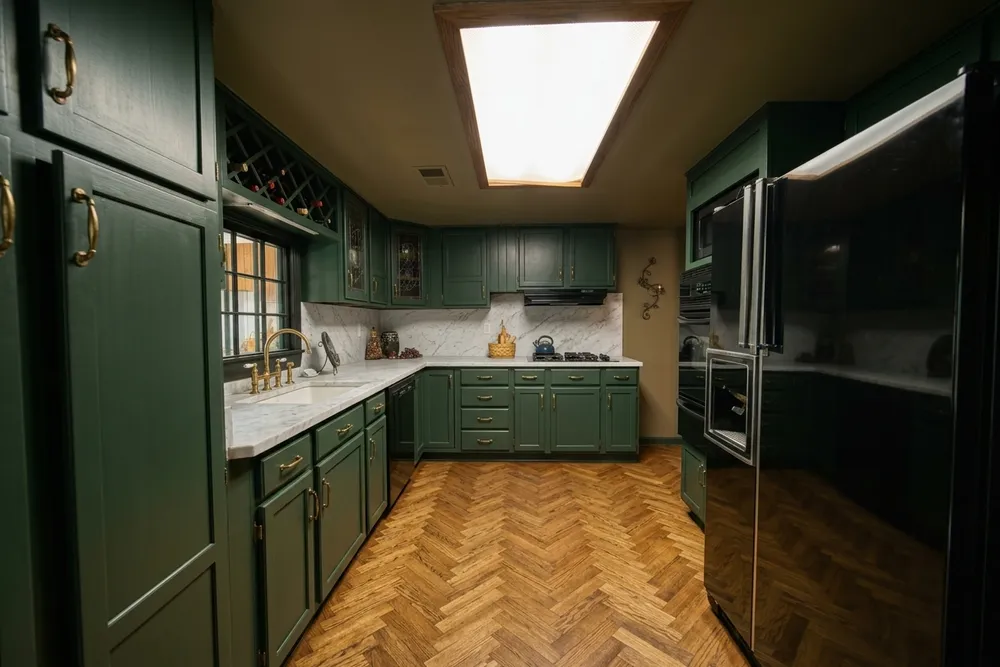 Dark forest green shaker cabinets with brass hardware, a white marble backsplash and a herringbone oak floor