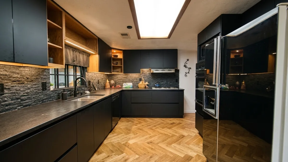 Matte black kitchen cabinets with a stone backsplash and a warm oak herringbone floor