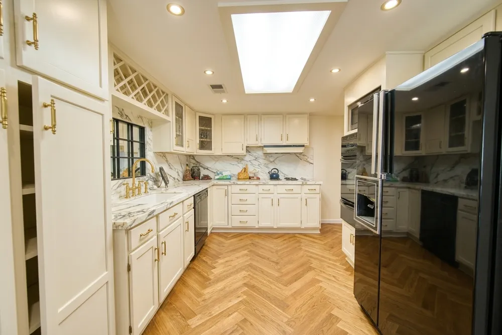 Traditional raised-panel ivory cabinets with brass hardware, a marble backsplash and a herringbone oak floor