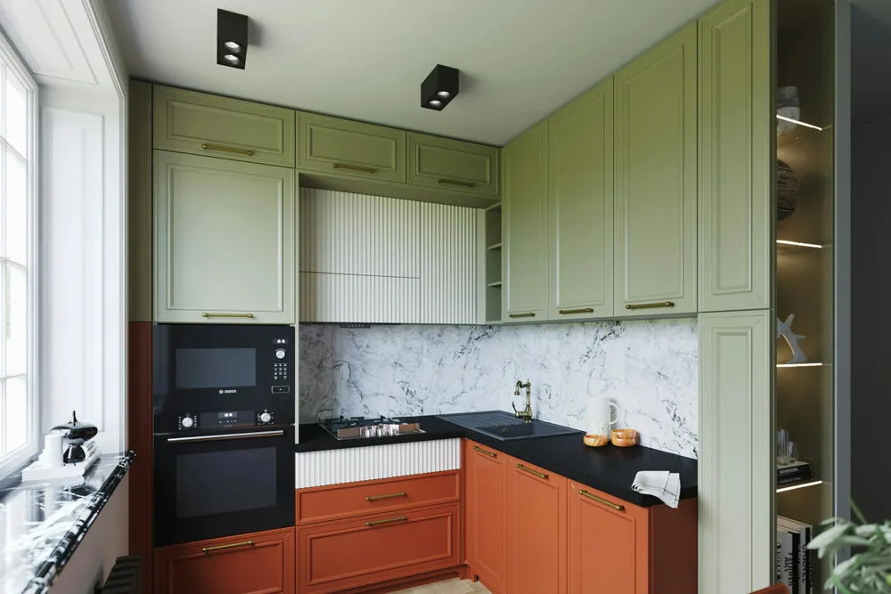 A corner kitchen with sage green upper cabinets, terracotta lower cabinets, brass bar pulls, a black countertop and a marble-look backsplash
