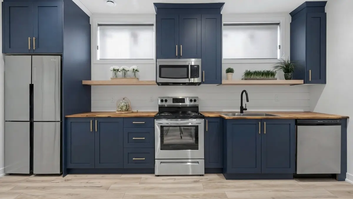 Navy shaker kitchen cabinets with brushed brass bar pulls, a butcher-block countertop, a white shiplap backsplash, open wood shelves between two windows and a light plank floor
