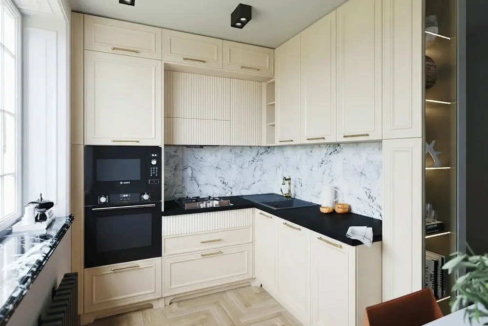 The same small kitchen with every cabinet in soft matte cream, raised-panel doors and brass pulls kept, and the black countertop, black sink, marble-look backsplash and herringbone floor unchanged