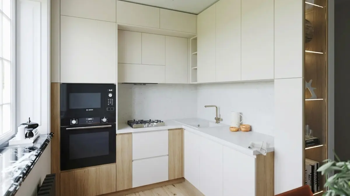 Small L-shaped kitchen with flat cream cabinets, oak panels beside the built-in oven and under the cooktop, a white countertop, a light plank floor and a window with a black marble sill