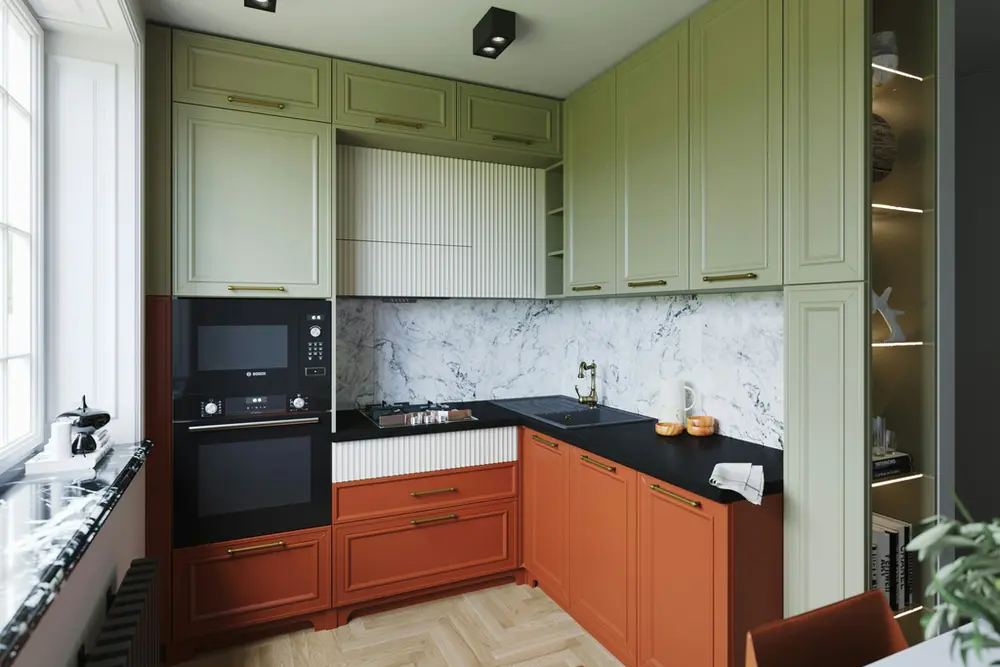 Small L-shaped kitchen with olive green raised-panel upper cabinets, terracotta base cabinets, brass bar pulls, a black countertop, a marble-look backsplash and an oak herringbone floor