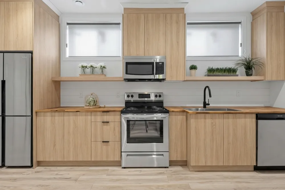 The same kitchen with light oak-look slab cabinets, a butcher-block countertop, a white shiplap backsplash and an extra tall cabinet at the right end