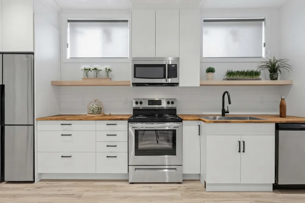 The same kitchen with flat white slab cabinets, black pulls, a butcher-block countertop, a white shiplap backsplash and pale wood open shelves