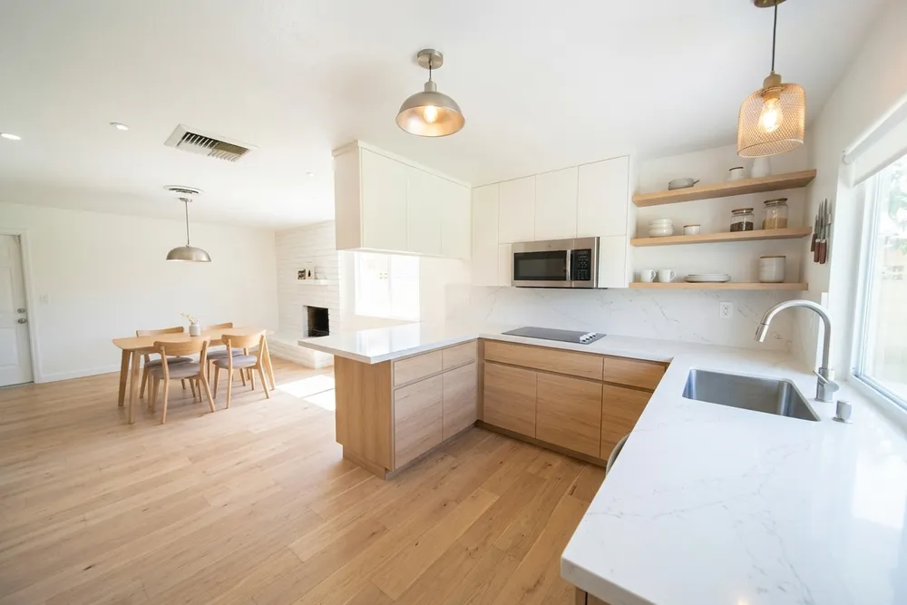 Flat-panel cool white kitchen cabinets with light oak open shelving, a white quartz countertop, and a wide-plank warm oak floor