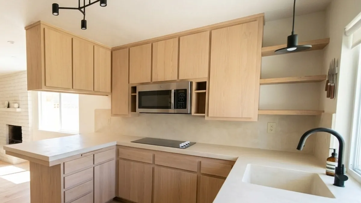 Flat-front light wood cabinets with open wood shelves, a cream plaster-look countertop and backsplash, a black faucet and a black pendant light