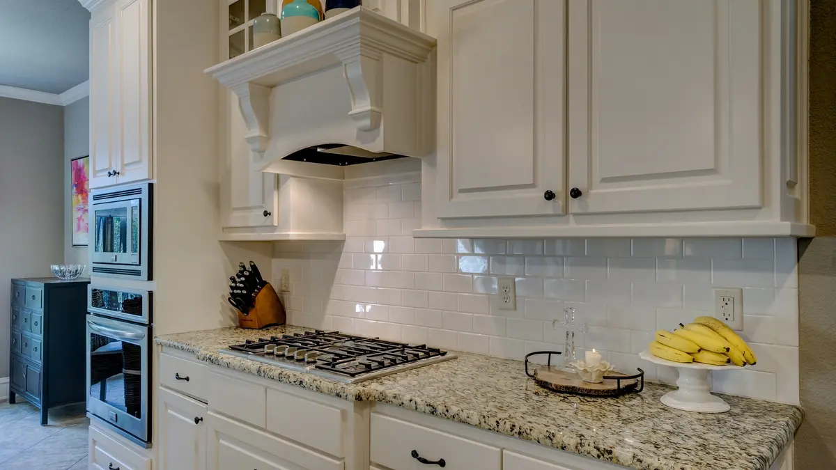 A white kitchen with raised-panel cabinets, a speckled granite countertop, white subway tile and a white range hood