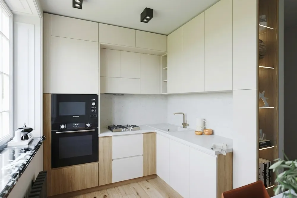Dezelfde hoekkeuken met warmwitte greeploze fronten, licht eiken onderkasten en een effen lichte achterwand
