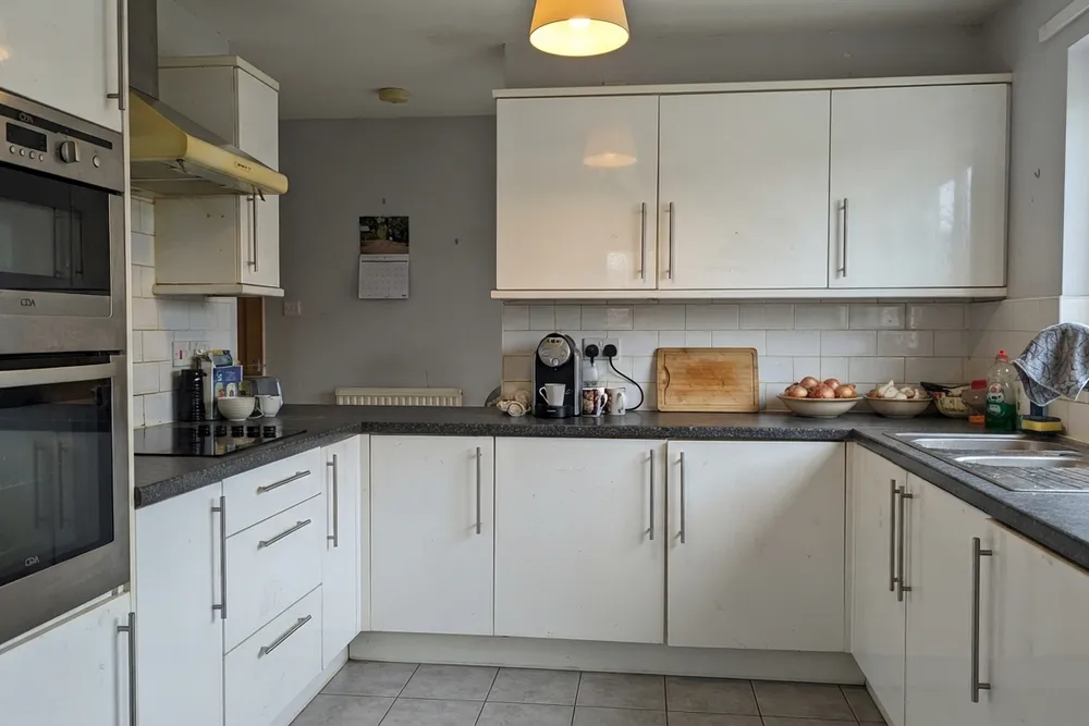 Een U-keuken met crème hoogglansfronten, stalen balkgrepen, een donker gespikkeld blad, crème metrotegels en grijze vloertegels