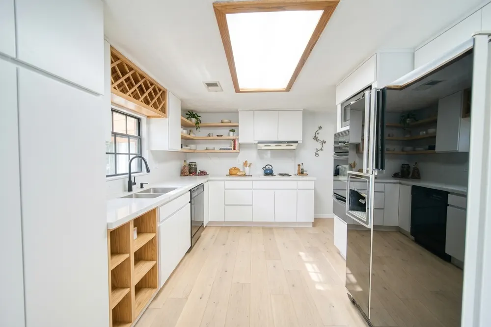 Dezelfde U-keuken in wit met open vakken onder het werkblad en een lichte houten vloer