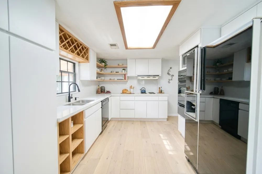 Dezelfde keuken met witte greeploze fronten, open eiken schappen en een lichte houten vloer, in exact dezelfde opstelling