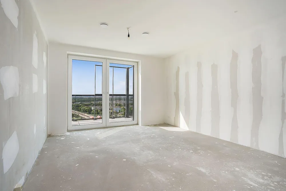 Kale ruimte zonder keuken, met kaal stucwerk, een betonnen vloer en een grote deur naar het balkon