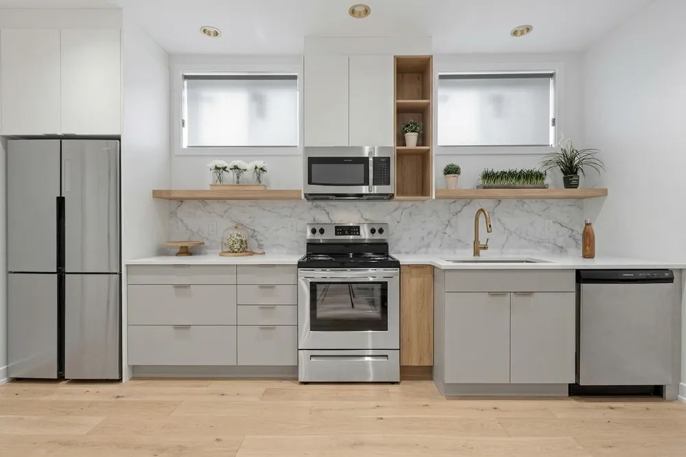Dezelfde keuken met warm witte greeploze fronten, een wit werkblad en een marmerlook achterwand
