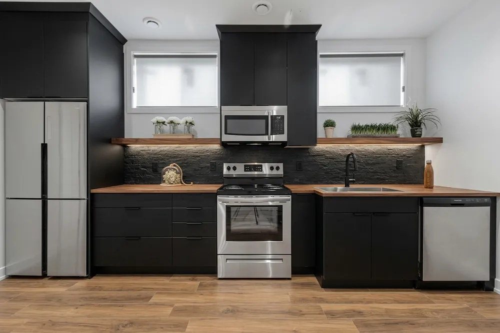 Dezelfde keuken met matzwarte fronten, een houten werkblad en een donkere natuursteenlook achterwand
